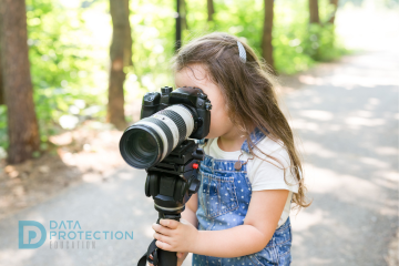 Photograph of a young girl taking a photo on a camera in a country lane. Data protection education logo is bottom left