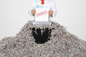 Hands of a man putting some paper marked confidential through a shredder sitting on a pile of shredding. Data Protection Education logo.