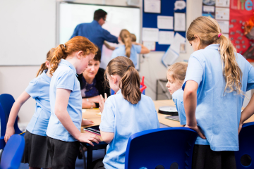 School children wearing blue shirts and grey skirts in a class room